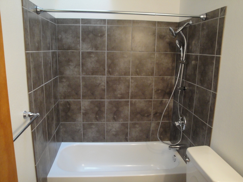 White bathtub surrounded by grey tile, with a wall-mounted shower and a curtain rod