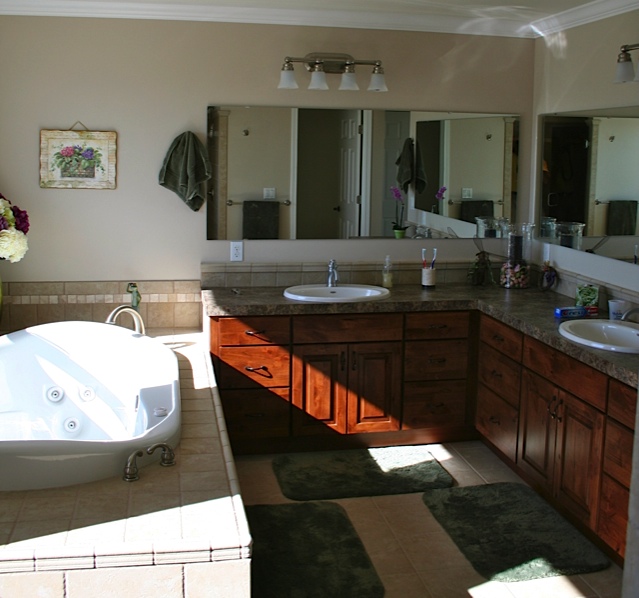 Friendship Builders bathroom project with warm wood vanities, broad mirrors and a white soaking tub