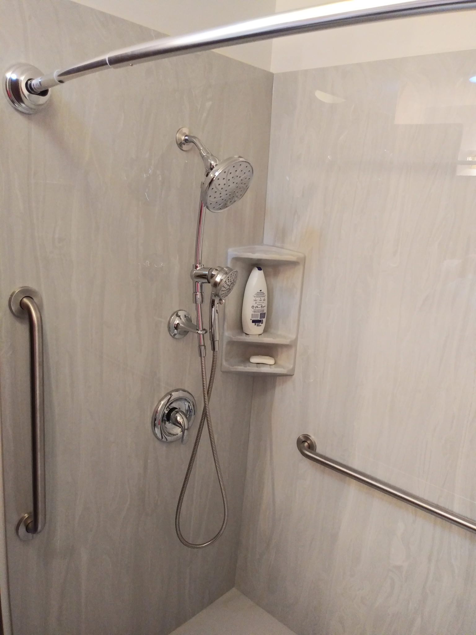 Vertical grab bar beside a handheld shower on a rail, a lever control, and recessed wall storage